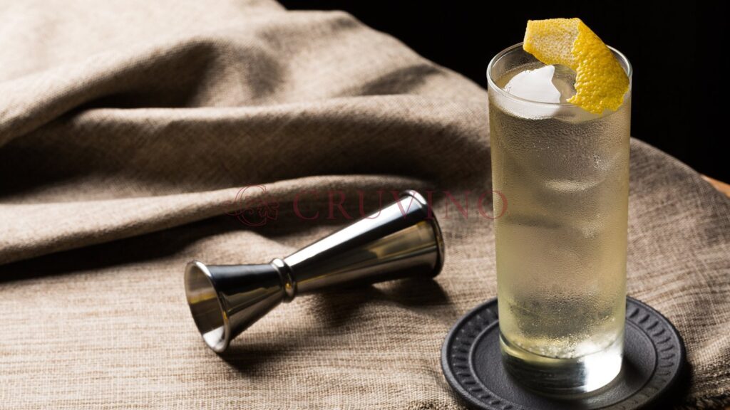 Highball z whisky, lodem i skórką cytryny obok miarki barmańskiej